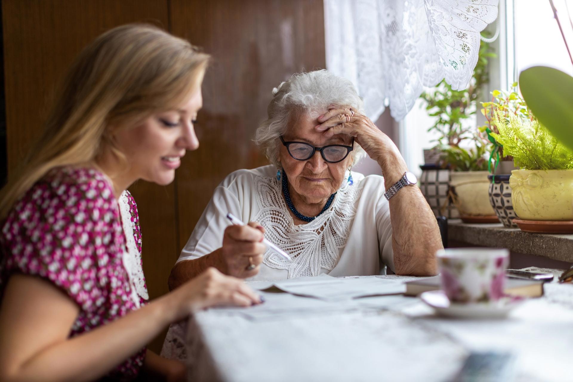 A medical social worker helping a senior woman work through paperwork at her kitchen table