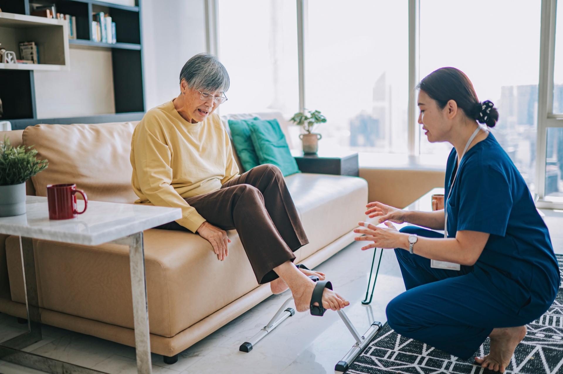 An occupational therapist guiding a senior woman through a gentle leg exercise in her living room