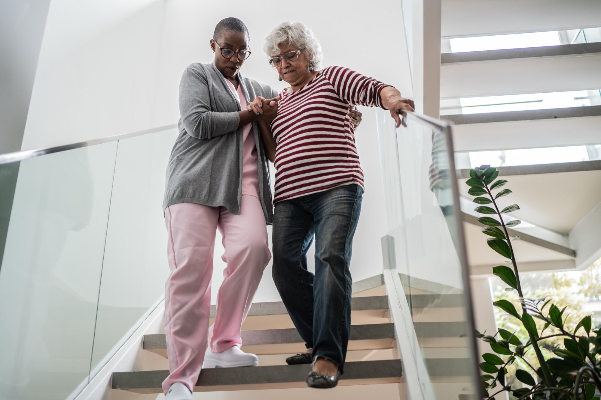 A physical therapist steadying a senior woman as she practices walking down the stairs at home